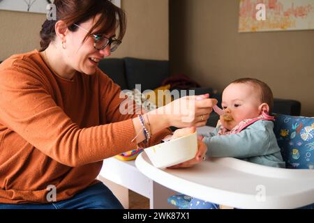 Mère nourrissant sa petite fille de 6 mois avec de la purée de légumes. Banque D'Images
