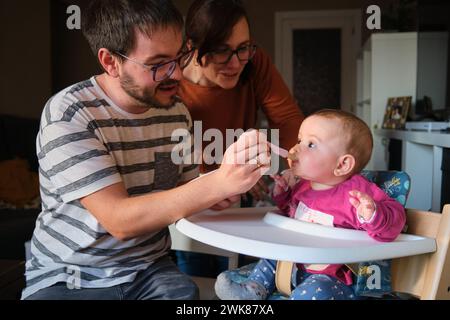 Parents nourrissant sa petite fille de 6 mois avec de la purée de fruits pour bébé. Banque D'Images