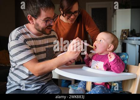 Parents nourrissant sa petite fille de 6 mois avec de la purée de légumes. Banque D'Images