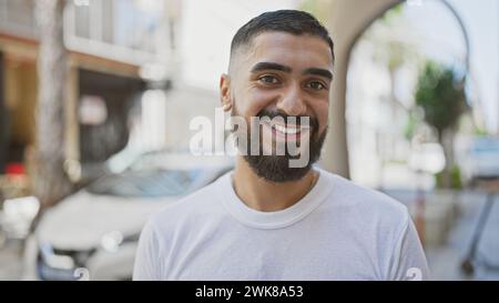 Bel homme barbu souriant à l'extérieur dans une ville, représentant le style de vie urbain et la positivité. Banque D'Images