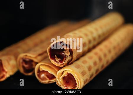 Petits pains de gaufrettes sucrés avec du lait condensé au chocolat sur fond sombre Banque D'Images