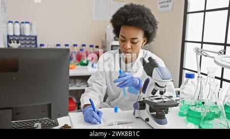 Scientifique afro-américaine analysant des échantillons dans un laboratoire intérieur, entourée d'équipements scientifiques. Banque D'Images