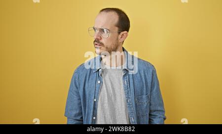 Portrait d'un homme hispanique barbu, chauve et spectaculaire dans une chemise en denim sur fond jaune, montrant la diversité et la modernité. Banque D'Images