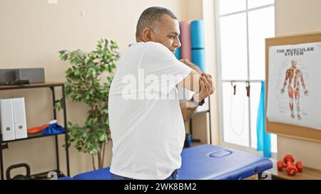 Un homme hispanique d'âge moyen exerce son coude dans une clinique de physiothérapie, décrivant la santé et la récupération. Banque D'Images