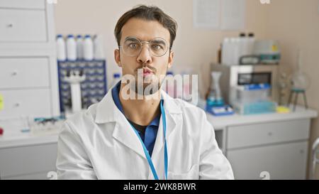 Bel homme hispanique à la barbe portant des lunettes et une blouse de laboratoire posant dans un cadre de laboratoire Banque D'Images