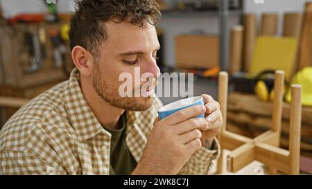 L'homme barbu profite d'une pause café dans un studio de menuiserie, capturant son style décontracté et son ambiance artisanale intime. Banque D'Images