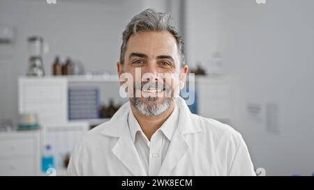 Jeune homme hispanique confiant, un scientifique souriant aux cheveux gris, debout dans le laboratoire, naviguant avec élégance dans la recherche médicale. Banque D'Images