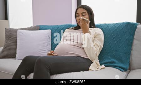 S'attendant à une jeune femme, se relaxant confortablement sur le canapé de son salon, touchant tendrement son ventre enceinte pendant l'envoi, prononce un message vocal sincère Banque D'Images