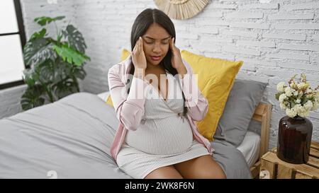 Stressé jeune femme hispanique, attendant la mère, est assise sur son lit, anxieuse et fatiguée, souffrant d'un grave mal de tête dans le matin tranquille de son apar Banque D'Images