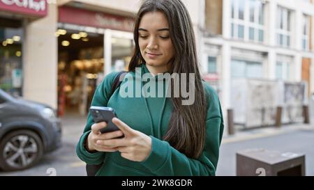 Une jeune femme hispanique utilise son smartphone dans une rue animée de la ville, incarnant la vie urbaine et la technologie. Banque D'Images