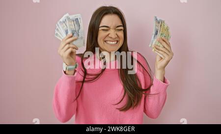 Jeune femme heureuse tient les semelles péruviennes avec un clin d'œil contre un mur rose, montrant richesse et joie. Banque D'Images