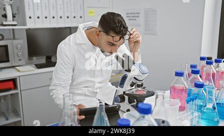 Un homme dans un laboratoire examine des échantillons à travers un microscope entouré de tubes à essai, transportant la recherche et la science. Banque D'Images