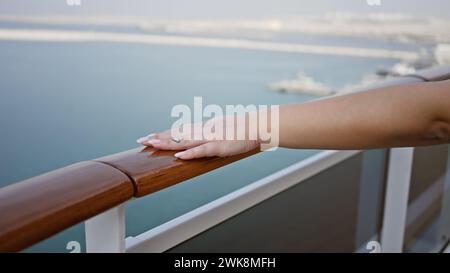 Vue rapprochée de la main d'une femme reposant sur la balustrade d'un pont de bateau de croisière avec l'horizon océanique en arrière-plan. Banque D'Images