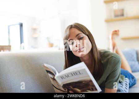Une jeune femme caucasienne aime lire un magazine tout en se relaxant sur un canapé Banque D'Images