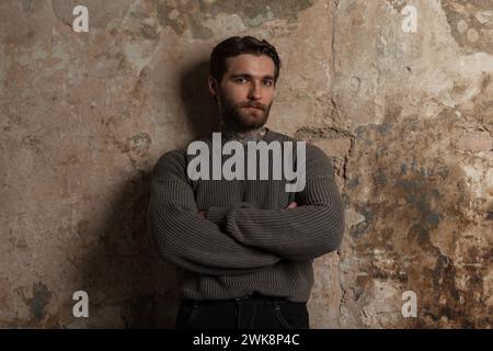 Brutal succès beau Hipster homme avec Une coiffure et barbe dans Un pull Vintage de mode se tient près D'Un mur de Grunge en béton Banque D'Images