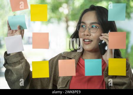 Femme d'affaires ayant des idées sur la stratégie de marketing au bureau, des idées sur le mur de verre avec des notes adhésives. Banque D'Images
