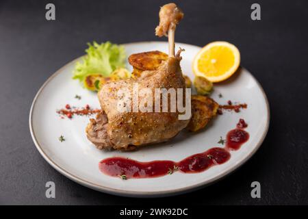 Cuisse de canard confite avec choux de Bruxelles, pommes de terre au four, thym, orange et sauce aux airelles. Cuisine française traditionnelle. Mise au point sélective, gros plan. Banque D'Images