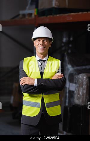 Homme souriant en gilet de sécurité et casque de sécurité debout avec les bras croisés, tir de tête professionnel Banque D'Images