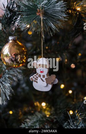 Une petite décoration de bonhomme de neige en bois suspendue à un arbre de Noël familial avec des lumières de fée brillantes. Banque D'Images