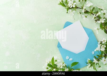 Joyeuses Pâques. Carte de papier blanc vierge dans une enveloppe bleue, oeufs en chocolat, cerisier frais ou fleurs de pommier sur fond vert. Carte de voeux de Pâques de printemps Banque D'Images