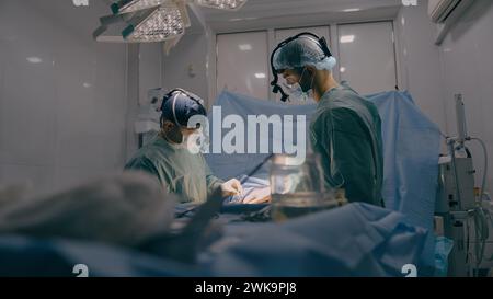 Équipe de deux médecins hommes chirurgiens traitant l'opération chirurgicale à l'aide d'instruments médicaux endoscopiques dans la salle d'opération stérile d'urgence hospitalière Banque D'Images