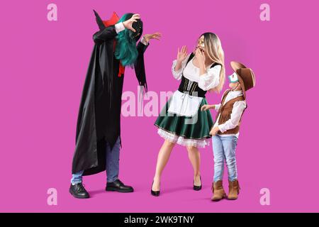 Père en costume de vampire effrayant sa famille en masques de carnaval sur fond violet Banque D'Images