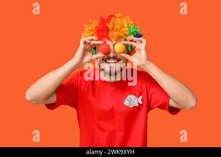 Beau jeune homme dans le déguisement drôle de clown sur fond orange. Fête du fou d'avril Banque D'Images