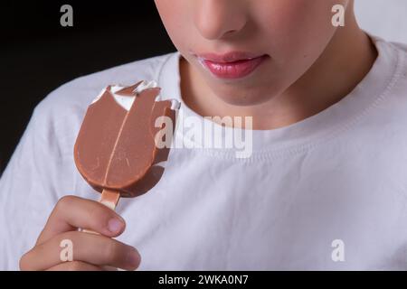 Un garçon dont le visage est méconnaissable mange de la crème glacée recouverte de chocolat. Banque D'Images