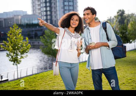 Photo de jeune petite amie pointant du doigt loin dans une atmosphère urbaine en utilisant des smartphones choisissant un restaurant pour visiter avec son petit ami Banque D'Images