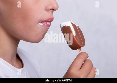 Un garçon dont le visage est méconnaissable mange de la crème glacée recouverte de chocolat. Banque D'Images