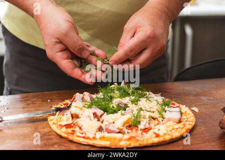 Saupoudrez les herbes sur la pizza. Les mains masculines ajoutent de l'aneth à la pizza. Banque D'Images