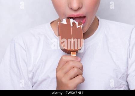 Un garçon dont le visage est méconnaissable mange de la crème glacée recouverte de chocolat. Banque D'Images