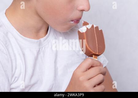 Un garçon dont le visage est méconnaissable mange de la crème glacée recouverte de chocolat. Banque D'Images