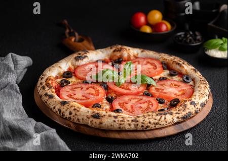 Pizza garnie de tomates, olives noires et basilic Banque D'Images