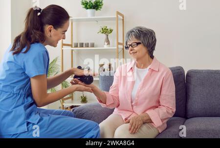 Amicale infirmière souriante tenant la balle en caoutchouc et faisant le massage des mains à la femme âgée heureuse Banque D'Images