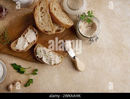 Pâté maison, tartinade ou mousse dans un pot en verre avec du pain tranché et des herbes avec des pignons de pin, fond de béton léger. Banque D'Images