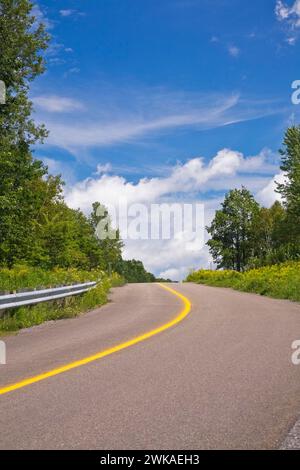 Route de campagne sinueuse en été avec une ligne de circulation jaune continue divisant indiquant une zone interdite de passage. Banque D'Images
