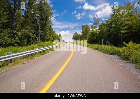 Route de campagne sinueuse en été avec une ligne de circulation jaune continue divisant indiquant une zone interdite de passage. Banque D'Images