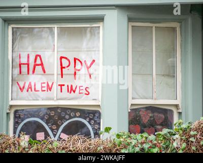Un signe 'Happy Valentines' peint à la main fait dans un script rouge affiché dans une fenêtre de maison Banque D'Images