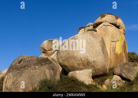 Grand rocher dans un champ par pente de montagne sous ciel bleu Banque D'Images