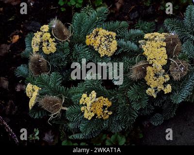 Arrangement décoratif de tombes automnales composé de branches de sapin vert, de fleurs jaunes séchées de la flèche et de taches sèches cartes rustiques marron en piquant. Main Banque D'Images