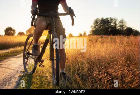 Cycliste professionnel roule sur un chemin de terre par une journée ensoleillée d'été. Vélo de gravier hors route. Banque D'Images