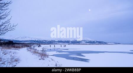 Les gens patinent sur la glace à Laugarvatn, en Islande, alors qu'une pleine lune se lève Banque D'Images