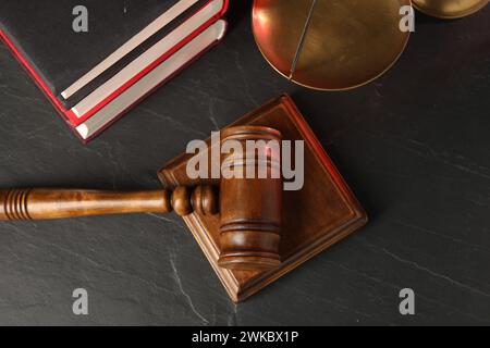 Marteau en bois, bloc sonore et livres sur table texturée sombre, pose à plat Banque D'Images