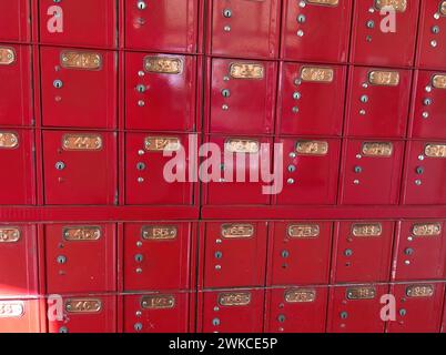 Rangées de boîtes postales vintage en métal rouge sur un mur dans le bureau de poste avec des étiquettes de numérotation en laiton Banque D'Images