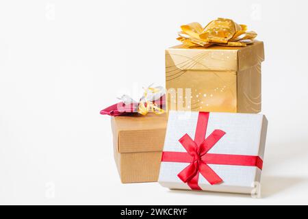 Trois boîtes-cadeaux enveloppées dans du papier et attachées avec ruban et noeuds sur fond blanc. Copier l'espace. Vue de face. Couleurs rouge, blanc et doré Banque D'Images