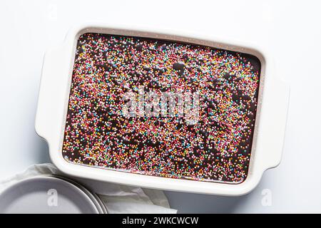 Gâteau au chocolat classique avec des saupoudrages colorés dans un plat de cuisson blanc, vue de dessus. Banque D'Images
