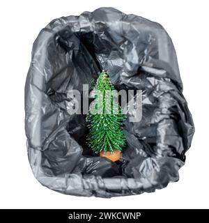 Vue de dessus d'une petite figurine de sapin de Noël jouet placée à l'intérieur d'une poubelle avec un sac en plastique noir. Options de recyclage et d'élimination des arbres du nouvel an. Banque D'Images