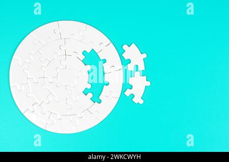 Vue de dessus en gros plan d'un puzzle circulaire vierge avec deux pièces manquantes mises de côté sur fond bleu clair. Banque D'Images