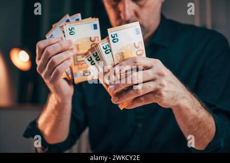 Homme d'affaires comptant cinquante billets en euros au bureau tout en travaillant des heures supplémentaires, focus sélectif Banque D'Images